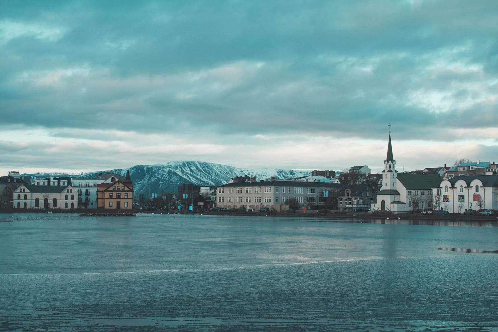 Colourful traditional Reykjavík houses reflected in the still wintry surface of Tjörnin lake under a soft blue-hour sky.
